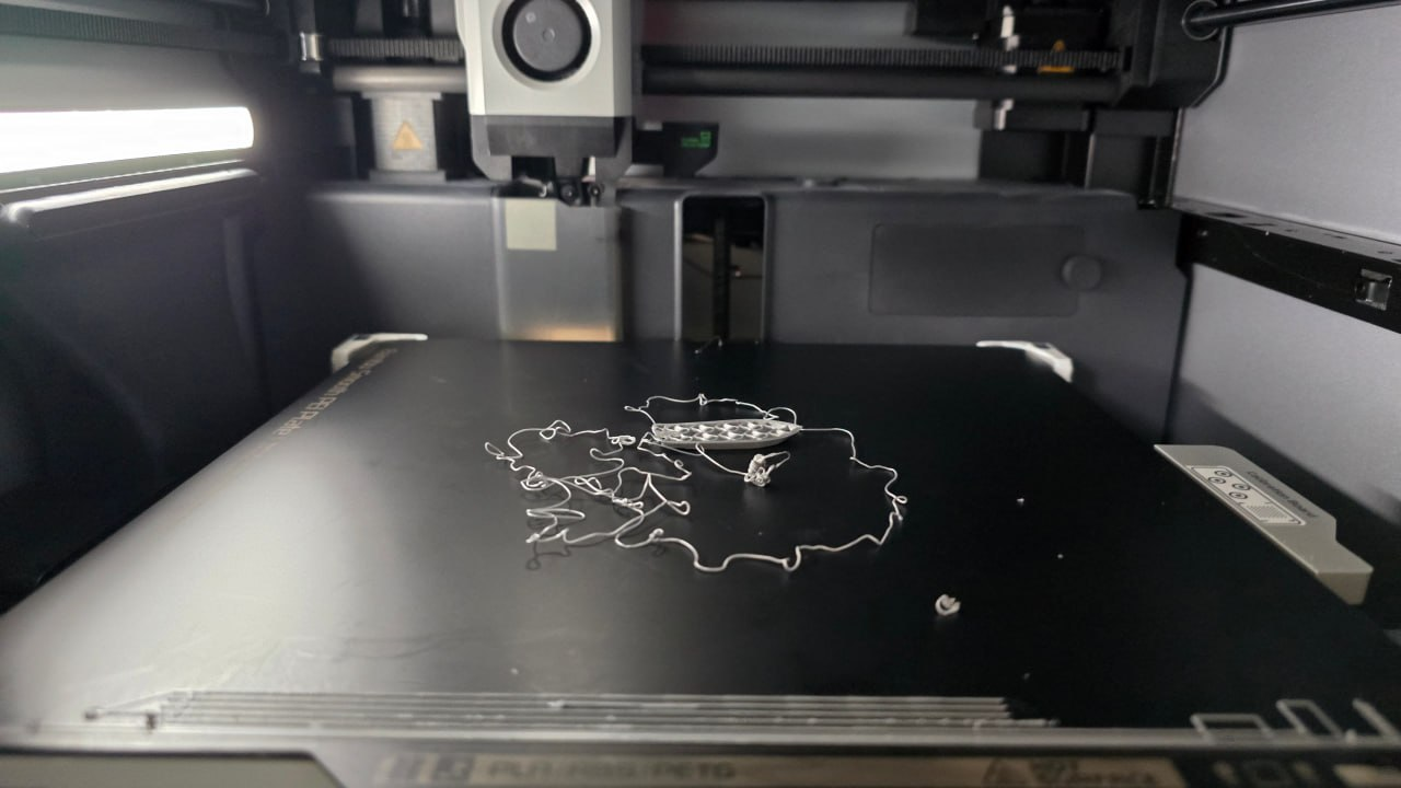 A failed first-layer print on a Bambu Lab X1C — the model popped off the bed leaving a tangled filament rat nest on the magnetic PEI plate