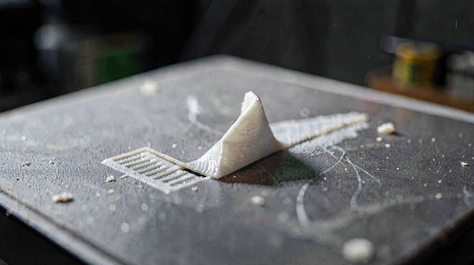 A 3D printed object on a build plate with one corner curling upward, demonstrating warping